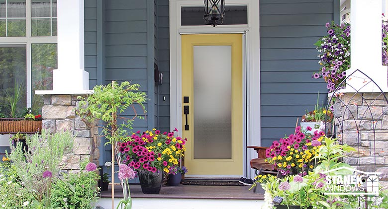 Dark wood front entry door Yellow entry door with full privacy glass on blue-gray houe with stone and wood pillars, brightly colored potted flowers.