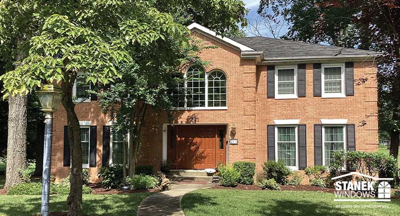 : A brick two-story home with double-hung windows, black shutters and special shape windows above the front door.
