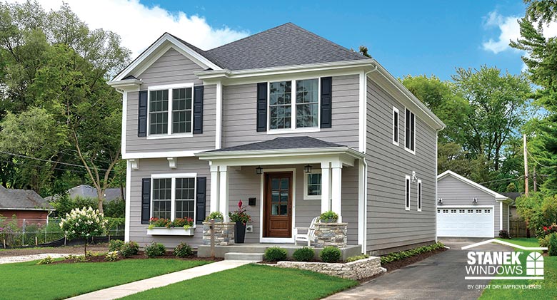 A two-story home with gray siding, double-hung windows, black shutters and a wood front door on a porch with white columns..