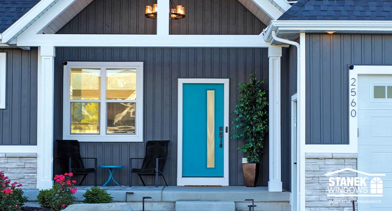 A modern entry door with a long, glass inset in bright blue adds a pop of color to a farmhouse style home with white trim. Entry Door